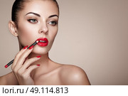 Beautiful woman paints lips with lipstick. Beautiful woman face. Makeup detail. Beauty girl with perfect skin. Red lips and nails manicure. Стоковое фото, агентство Ingram Publishing / Фотобанк Лори