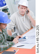 Two men at desk with calculator, phone and plans. Стоковое фото, агентство Ingram Publishing / Фотобанк Лори