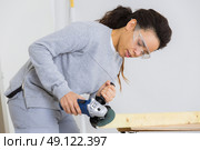 young adult female worker grinding plank with electric grinder. Стоковое фото, агентство Ingram Publishing / Фотобанк Лори