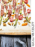 Green Asparagus wrapped in Parma ham with tomatoes, parmesan, Walnut  and dried apricot , ready for cooking, close up. Стоковое фото, агентство Ingram Publishing / Фотобанк Лори