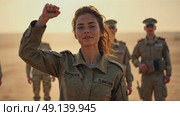 A woman in a military uniform stands tall, her right arm is raised in a fist pump after a successful mission. The background filled with tired but Happy colleagues in the military. Стоковое AI-видео, аниматор Sergey Grishin / Фотобанк Лори