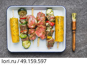 Meat, vegetables and corn Skewers in  green herbs rubs and Marinades with Brush on gray concrete background, top view. Стоковое фото, агентство Ingram Publishing / Фотобанк Лори
