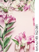 Florist workspace. Female hands holding beautiful pink lily flowers on pastel table with  florist decoration equipment, top view, frame. Creative Flowers arrangement. Invitation and holiday, concept. Стоковое фото, агентство Ingram Publishing / Фотобанк Лори
