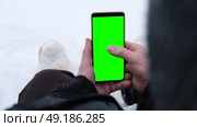 Young man sitting and holding smartphone with green screen outdoors in winter. Vertical mockup of mobile phone. Guy using phone with blank green display background. Smartphone with chromakey. Close-up. Стоковое видео, видеограф Евгений Демидюк / Фотобанк Лори