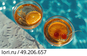 Two glasses filled with orange slices and cherries placed next to a swimming pool. Стоковое AI-изображение, AI-художник Данила Большаков / Фотобанк Лори