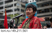 Mature woman confidently stands in front of a microphone, preparing to speak or perform. The setting appears to be a public event or presentation. Стоковое AI-изображение, AI-художник Данила Большаков / Фотобанк Лори
