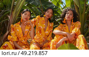 Three fashion models pose confidently in coordinating yellow floral outfits, surrounded by lush green plants. Стоковое AI-изображение, AI-художник Данила Большаков / Фотобанк Лори