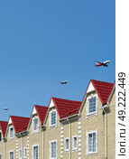 Surreal aerial view: Red-roofed cottages with low-flying passenger planes in formation, optical illusion, minimalist blue sky. Стоковое фото, фотограф Елена  Попкова / Фотобанк Лори