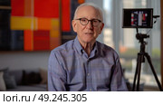 An older man seated in front of a camera, appearing focused and ready for a video recording or interview session. Стоковое AI-изображение, AI-художник Данила Большаков / Фотобанк Лори