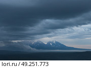 Вид на вулканы в сумерках. Красивый вечерний пейзаж. Пасмурная погода. Низкие облака. Природа полуострова Камчатка. Путешествия и туризм на Дальнем Востоке России. Камчатский край. Стоковое фото, фотограф Андрей Степанов / Фотобанк Лори