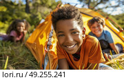 A group of children laying in the grass next to a colorful tent, enjoying the outdoors on a sunny day. Стоковое AI-изображение, AI-художник Данила Большаков / Фотобанк Лори