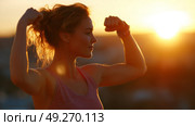 Woman celebrates strength with raised arms during sunset at a scenic overlook. Стоковое AI-изображение, AI-художник Сергей Толмачёв / Фотобанк Лори