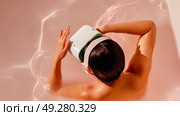 Person in pink-tinted water wears virtual headset, blending futuristic technology with spa-like relaxation in a surreal immersive scene. Стоковое AI-изображение, AI-художник Александра Троицкая / Фотобанк Лори