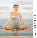 Woman practicing yoga on sea beach, stretching in an asymmetrical seated asana Parivritta Janu Sirsasana. Стоковое фото, фотограф Яков Филимонов / Фотобанк Лори