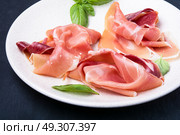 sliced ham served on dish. Sliced of Traditional Spanish jamon on a dark stone background. Стоковое фото, агентство Ingram Publishing / Фотобанк Лори