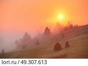 Sunrise over mountain field. Haystacks in misty rural hills. Foggy autumn morning in mountains. Стоковое фото, агентство Ingram Publishing / Фотобанк Лори