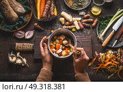 Female woman hands holding pan with diced colorful vegetables and a spoon on rustic kitchen table with vegetarian cooking ingredients and tools. Healthy and clean food  cooking and eating  concept. Стоковое фото, агентство Ingram Publishing / Фотобанк Лори