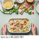 Woman female hands holding pasta casserole with romanesco cabbage and ham in creamy sauce, on kitchen table background with ingredients, top view, border.  Italian cuisine. Стоковое фото, агентство Ingram Publishing / Фотобанк Лори