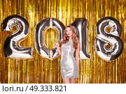 Beautiful Woman celebrating New Year. Girl with Glass of Champagne. Girl posing with Silver colored 2018 number Balloons over Golden sparkly background. Happy New Year. Стоковое фото, агентство Ingram Publishing / Фотобанк Лори
