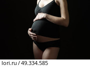 midsection of pregnant woman in black clothes on a black background. Стоковое фото, агентство Ingram Publishing / Фотобанк Лори