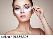 Portrait of Beauty Woman with eye Patches showing an effect of Perfect Skin. Beautiful Face of young Woman with clean Fresh Skin and bare shoulders on beige background. Brunette Spa Girl. Стоковое фото, агентство Ingram Publishing / Фотобанк Лори