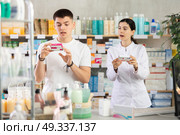 Interested young guy choosing between two boxes of paracetamol antipyretic pills and professional pharmacist woman helping and offering supplements at drugstore. Стоковое фото, фотограф Яков Филимонов / Фотобанк Лори