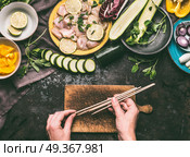Chicken meat and vegetables skewers making. Female hands holding wooden skewer on kitchen table background with chicken pieces and vegetables, top view. Grill preparation. Стоковое фото, агентство Ingram Publishing / Фотобанк Лори