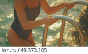Woman in swimsuit climbs ladder out of sea by rocky shore at warm sunset light. Стоковое видео, видеограф Ольга Сухарева / Фотобанк Лори