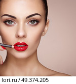 Beautiful Woman paints Lips with Lipstick. Beautiful Woman Face. Makeup detail. Beauty Model with Perfect Skin. Red Lips and Nails Manicure. Стоковое фото, агентство Ingram Publishing / Фотобанк Лори