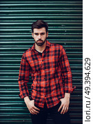 Young bearded man, model of fashion, wearing a plaid shirt with a green blind behind him. Guy with beard and modern hairstyle in urban background. Стоковое фото, агентство Ingram Publishing / Фотобанк Лори