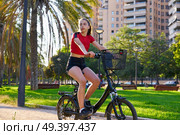 Girl riding e-bike in a city park with red t-shirt foldable ebike. Стоковое фото, агентство Ingram Publishing / Фотобанк Лори