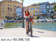 Girl riding a foldable e-bike in a Mediterranean marina port ebike. Стоковое фото, агентство Ingram Publishing / Фотобанк Лори
