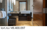 Bathroom. There is a white ceramic washbasin on the marble countertop, dispensers with soap, lotion. A banquette on the floor. The lamps are lit. Towels on the handrail. Reflection in the wall mirror. Стоковое фото, фотограф Вера Ивановна Кубарева / Фотобанк Лори