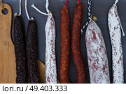 Cured meat and sausages hanging on black wooden background close up. Cured meat and sausages. Стоковое фото, агентство Ingram Publishing / Фотобанк Лори