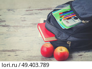 School backpack with supplies and apples on white desktop, retro toned. School backpack with supplies. Стоковое фото, агентство Ingram Publishing / Фотобанк Лори