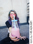 Happy beautiful teen with pink sunglasses cheers and enjoys a pink beverage sitting on urban ground. Стоковое фото, агентство Ingram Publishing / Фотобанк Лори