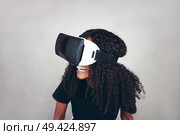 A beautiful young black woman with curly afro hair wears virtual reality VR headset and plays videogames while smiling in studio with grey background. Стоковое фото, агентство Ingram Publishing / Фотобанк Лори