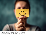 A woman smiling while holding a yellow piece of paper with a smiley face drawn on it. Стоковое AI-изображение, AI-художник Данила Большаков / Фотобанк Лори