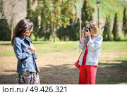 Two young tourist women taking photographs with analogic reflex camera in urban park. Travelers concept. Стоковое фото, агентство Ingram Publishing / Фотобанк Лори