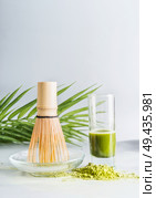 Matcha espresso in glass with whisk and matcha powder on table at light background, front view with copy space. Clean eating, detox beverage, healthy dairy food concept. Antioxidant boost drink. Стоковое фото, агентство Ingram Publishing / Фотобанк Лори