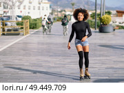 Young fit black woman on roller skates riding outdoors on urban street. Smiling girl with afro hairstyle rollerblading on sunny day. People ciclyng at background.. Black woman on roller skates riding outdoors on urban street. Стоковое фото, агентство Ingram Publishing / Фотобанк Лори