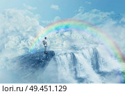 Young boy on a cliff looking at the horizon with a waterfall above clouds. Life journey below a rainbow in paradise. Inspirational imaginary view. . Стоковое фото, агентство Ingram Publishing / Фотобанк Лори