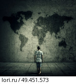 Man surrounded by limitations, daily routine, looking at the world map on a concrete wall. International travel cocept. Стоковое фото, агентство Ingram Publishing / Фотобанк Лори