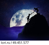 Man giving helping hand to friend to climb mountain rock cliff. Teamwork and trust concept in risky situation. Full moon night background. . Стоковое фото, агентство Ingram Publishing / Фотобанк Лори