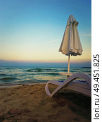 Beautiful sunset view as a deckchair with umbrella on the sand beach in front of a blue sea water. Стоковое фото, агентство Ingram Publishing / Фотобанк Лори