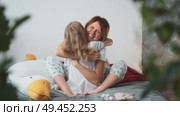 Embrace between parent and child in morning light on soft bed. Happy moment of security and unconditional care within cozy family space. Mother hugging blonde daughter, happy family concept. Стоковое видео, видеограф Енваев Андрей / Фотобанк Лори