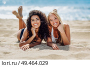 Two young women with beautiful bodies in swimwear on a tropical beach. Funny caucasian and arabic females wearing black and white swimsuits lying on the sand on the beach. Two young women with beautiful bodies in swimsuit on a tropical beach. Стоковое фото, агентство Ingram Publishing / Фотобанк Лори