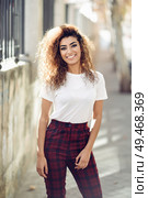 Beautiful young arabic woman with black curly hairstyle. Arab girl in casual clothes in the street. Happy female wearing white t-shirt and checked pants.. Arab girl in casual clothes in the street. . Стоковое фото, агентство Ingram Publishing / Фотобанк Лори