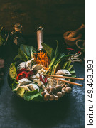 Tasty vegetarian Asian dumpling hot pot. Fresh colorful Asian food ingredients in wok pan with chopsticks on dark rustic kitchen table background. Стоковое фото, агентство Ingram Publishing / Фотобанк Лори
