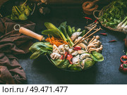 Preparation of korean hot pot . Wok pan with vegetables and dumplings  on dark rustic kitchen table background with ingredients, top view. Copy space. Стоковое фото, агентство Ingram Publishing / Фотобанк Лори